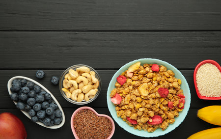 Granola with strawberries in a bowl with berries on black wooden background. Top view