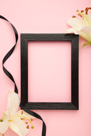 Beautiful lily flower with blank frame and black funeral ribbon on pink background. Verticalの写真素材