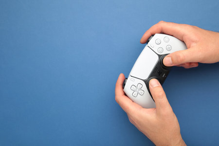 Mykolaiv, UKRAINE - July, 2024: Female hand holding a new Sony Playstation 5 controller on blue