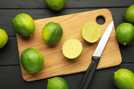 Green lime with cut in half on cutting board on black background. Top view