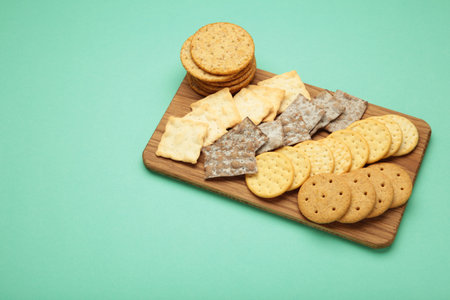 Different crackers on cutting board on mint background. Space for text. Top view