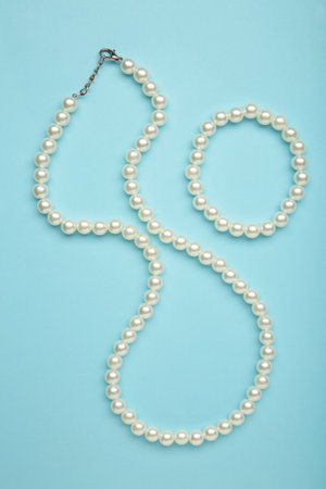 Elegant pearl necklace with bracelet on blue background, top view. Space for text