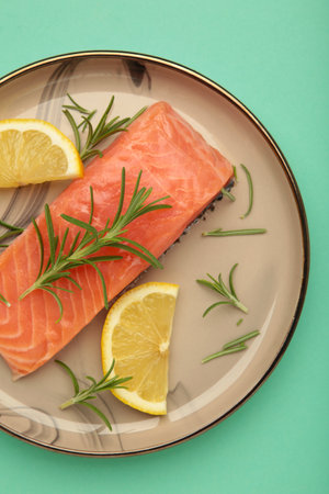 Red fish. Raw salmon fillet with rosemary and lemon on mint background. Top viewの写真素材