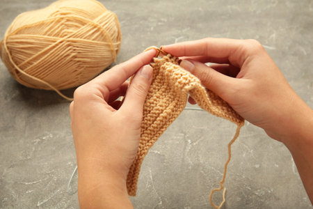 Women's hands knitting. Beige knitting yarns on gray background. Top view
