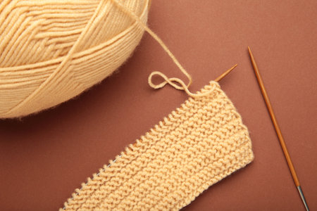 Different yarns, knitting needles on brown background. Top view