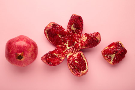 A whole pomegranate and a half-cut pomegranate with seeds on pink background.の写真素材