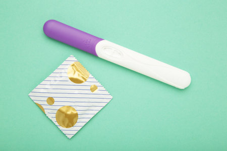 Pregnancy test with condom on mint background.