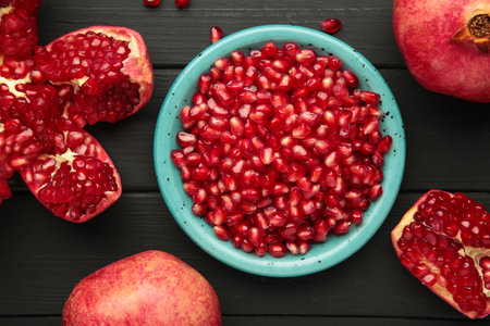Open pomegranates, and pomegranate seeds on black wooden background. Macro photoの写真素材