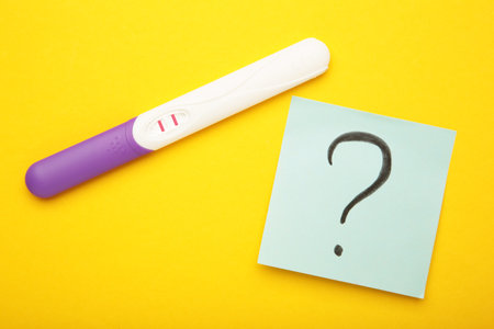 Pregnancy test with two stripes with question marks on yellow background. Top viewの写真素材