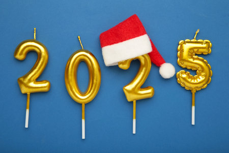 Holiday background Happy New Year 2025. Numbers of year 2025 made by gold candles with Santa hat on...