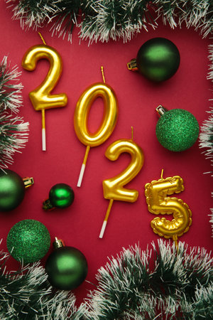 Merry Christmas and Happy New Year 2025. Golden candles numbers 2025 with green balls on red...