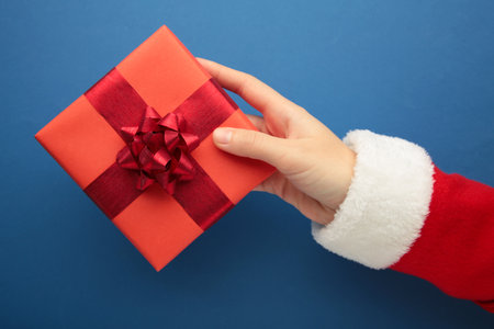 Top view of Santa's hands holding a red gift box on a blue background. Top viewの写真素材