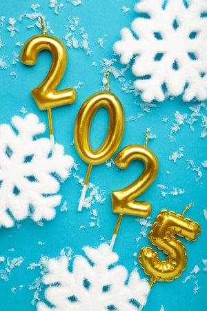 Numbers of year 2025 made by gold candles with snowflakes on blue background. Top viewの写真素材