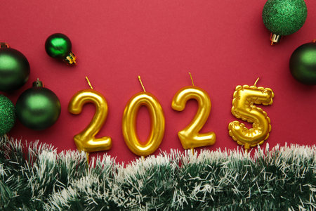 Holiday background Happy New Year 2025. Numbers of year 2025 made by gold candles with Christmas green toy on red background.の写真素材