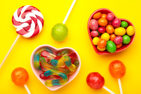 Different types of candies on yellow background, copy space. Colorful birthday party background.