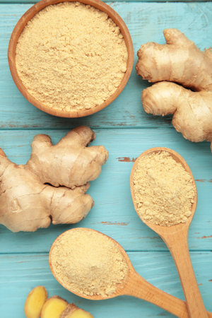 Wooden spoon with dried ginger powder and fresh ginger root on blue wooden background.の写真素材