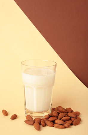 Fresh almond milk in glass and almonds on beige background. Healthy vegan plant based alternative milk replacer.の写真素材