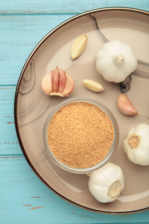 Fresh garlic and garlic powder on plate on blue background. Using spices for meals.の写真素材