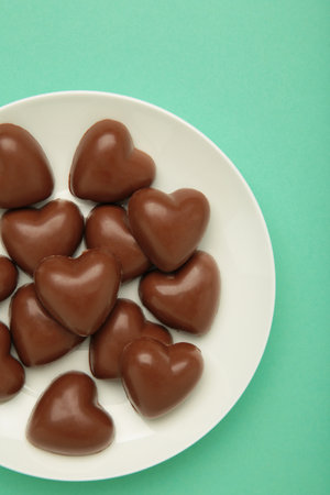 Red chocolate sweets as heart on plate on mint background. Valentine's day concept. Verticalの写真素材