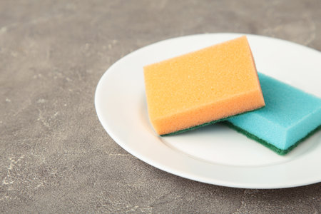 Cleaning sponge with plate on gray concrete background. Space for text
