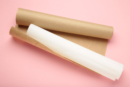 Rolls of white and brown baking paper on pink background. Top view