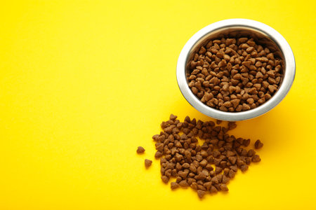Dog or cat food in a silver bowl on yellow background. Top view