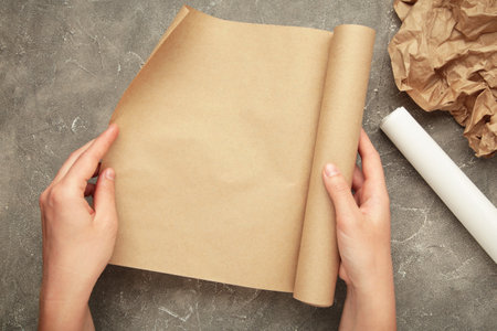 Female hands with roll of baking paper on gray concrete background. Top view