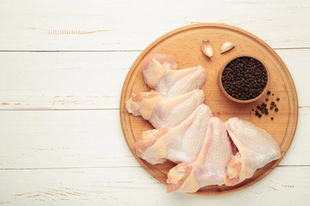 Raw chicken pieces with ingredients for cooking on wooden cutting board on white wooden, top viewの写真素材