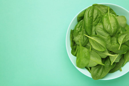 Baby spinach leaves with water drops in mint bowl on mint background. Raw organic spinach greens. Top viewの写真素材