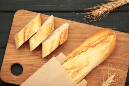 Baguette whole and cut into pieces on cutting board on black background. Space for text