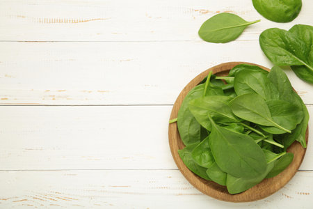Spinach leaves in a wooden plate on white wooden background. Top view.の写真素材
