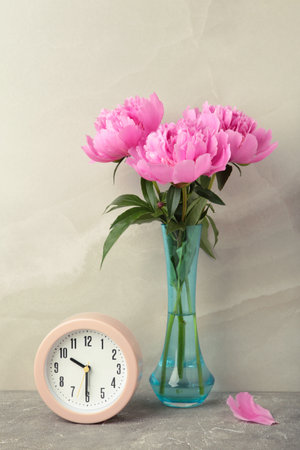 Romantic background with alarm clock and pink peonies on gray background. Vertical photo. Top viewの写真素材