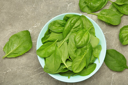 Spinach leaves in mint plate on gray concrete background. Top view.