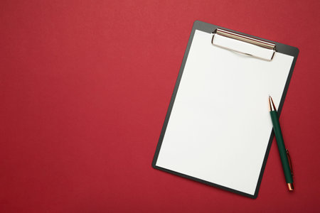 Black tablet with piece of empty paper and pen on red background. Top viewの写真素材