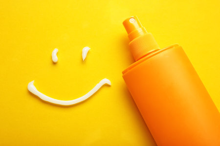 Sunscreen on yellow background. Plastic bottle of sun protection and white cream in the shape of...