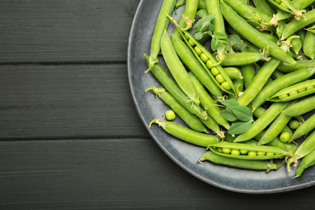 Fresh green peas in plate with pods and leaves on black wooden background. Top viewの写真素材