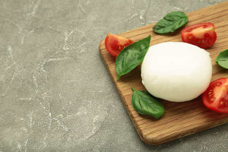 Mozzarella cheese with green basil leaves and tomato on cutting board on gray background. Space for textの写真素材