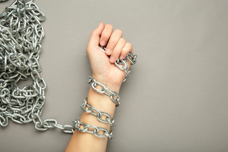 Hands are chained in chains on gray background. Top view