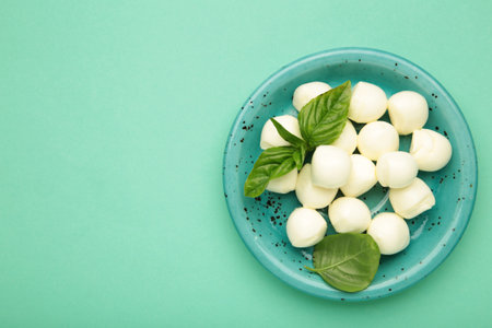 Mini mozzarella with green basil on mint background. Top viewの写真素材