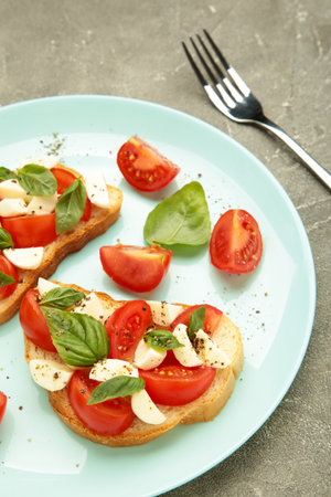 Italian Caprese salad with cherry tomatoes, mozzarella, basil on mint plate on gray background. Vertical photoの写真素材