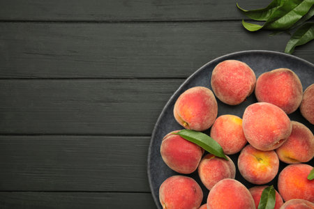 Sweet peaches and leaves on dark plate on black wooden background. Top viewの写真素材