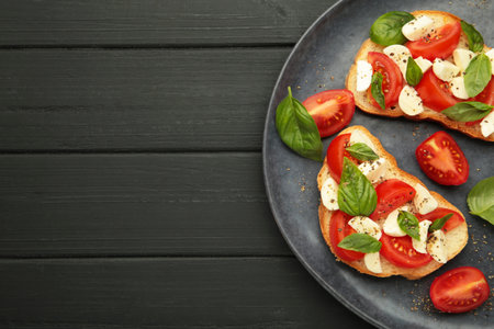Tasty sandwich with mozzarella cheese, tomatoes and basil on dark plate on black wooden background.の写真素材