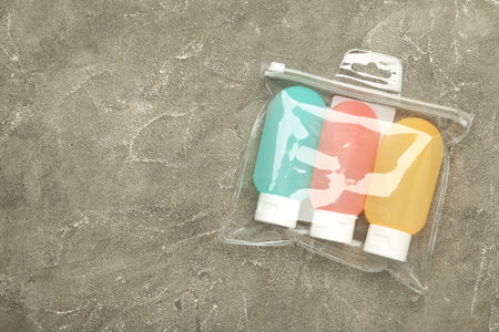 Transparent bag with travel bottles with body care cosmetics on gray concrete background. Top view