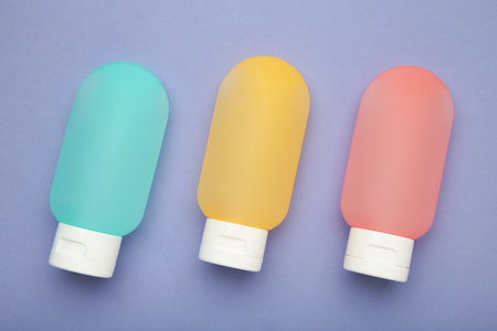 Travel bottles with body care cosmetics on purple background. Top view