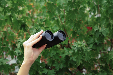 Female hand holds black binoculars. Looking through binoculars, journey, find and search concept