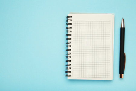 Notebook and pen on blue background. Top view