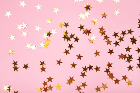 Golden glitter stars on pink background. Top view