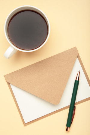 Craft envelope with a cup of coffee on beige background. Top view