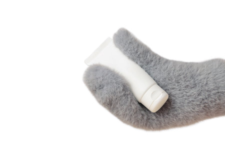 Winter skincare concept with a hand in gray mitten holding a white moisturizing cream, surrounded by soft snow. Isolated photoの写真素材