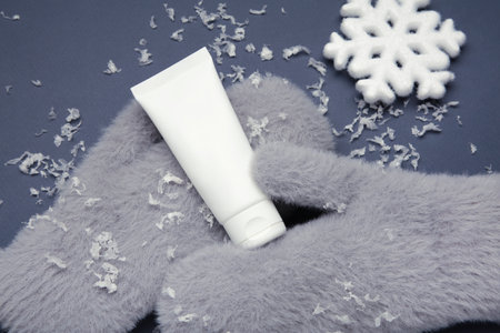 Winter skincare concept with gray mitten and moisturizing cream, surrounded by soft snow. Top viewの写真素材